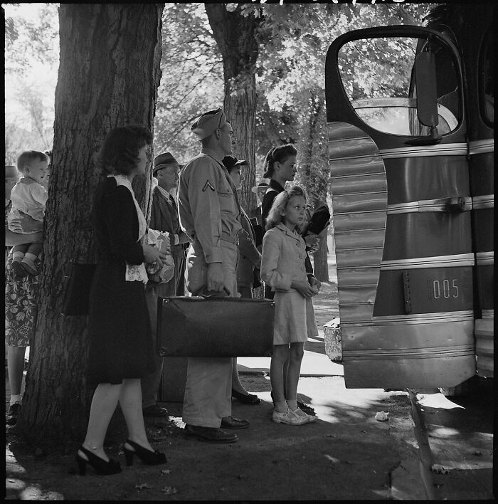 Colorized historical photo showing a group of people including a soldier boarding a vintage bus under autumn trees.
