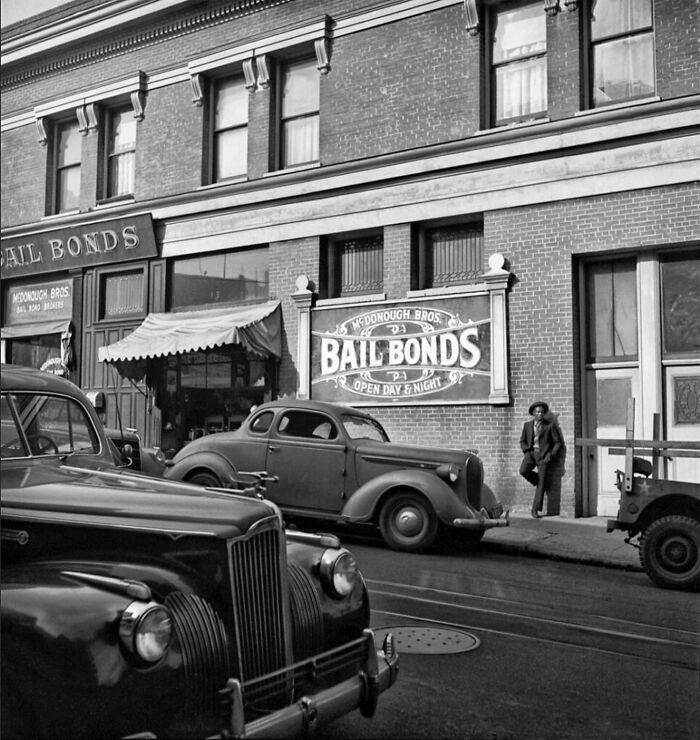 Colorized historical photo showing vintage cars parked by a McDonough Bros Bail Bonds building on a sunny street.