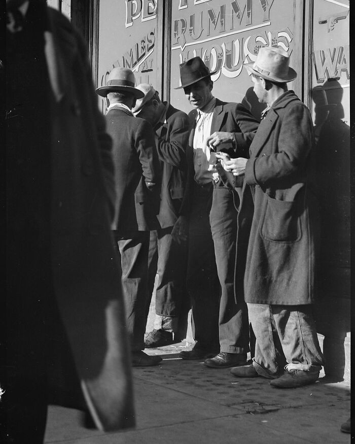 Group of men wearing hats and coats standing outside a building, colorized historical photo by a viral artist.
