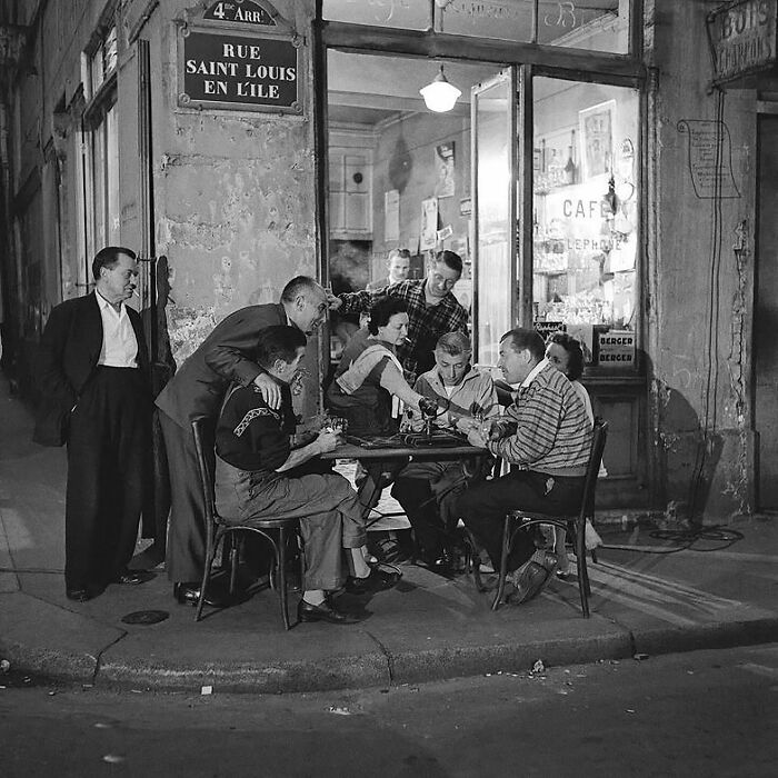 Colorized historical photo of people socializing outside a Paris cafe at night, showcasing magical historical moments recreated.