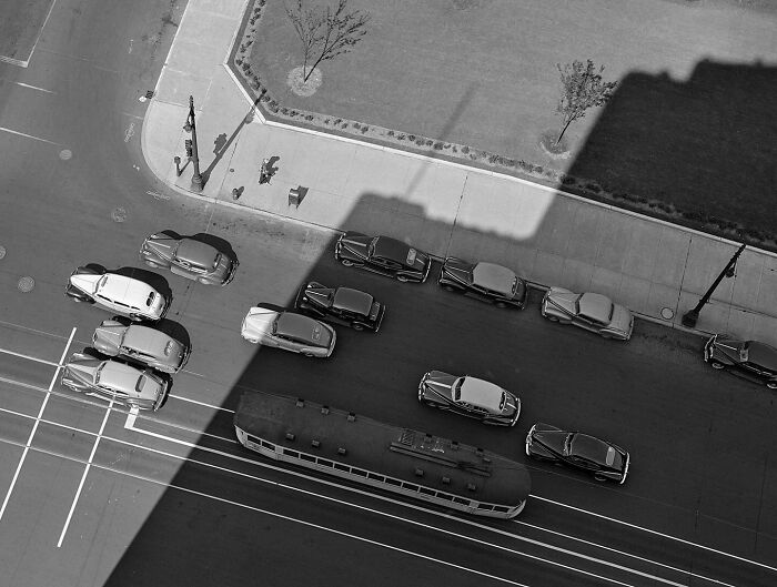 Colorized historical photo showing vintage cars and a tram on a city street from a top-down perspective.