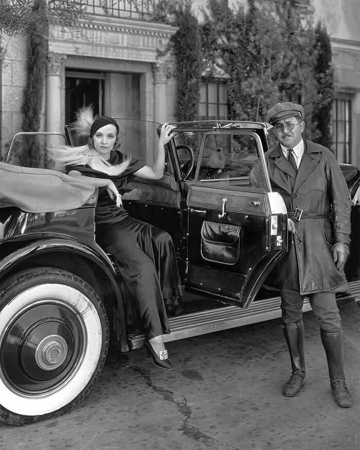 Colorized historical photo of a woman in red dress and a man in leather jacket by a vintage car, showcasing magical colorized art.