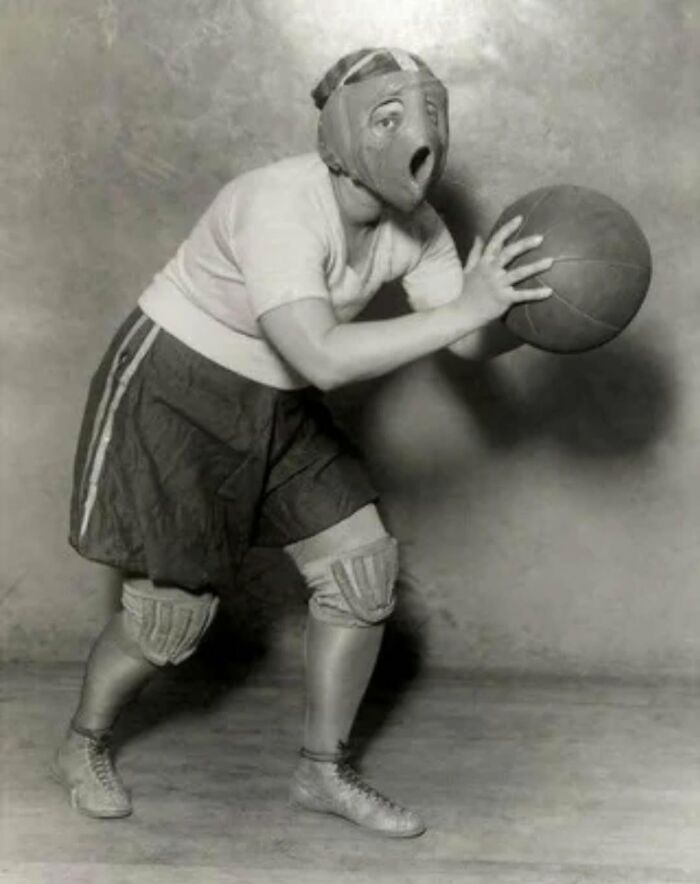 Vintage basketball player wearing old protective gear and holding a basketball in a historical sports setting.