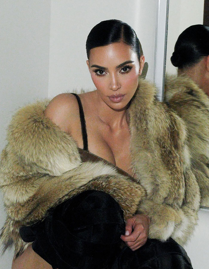 Kim Kardashian wearing a fur coat posing in front of a mirror with discussions about plastic surgeries around her. Kim Kardashian wearing a fur coat posing in front of a mirror with discussions about plastic surgeries around her.