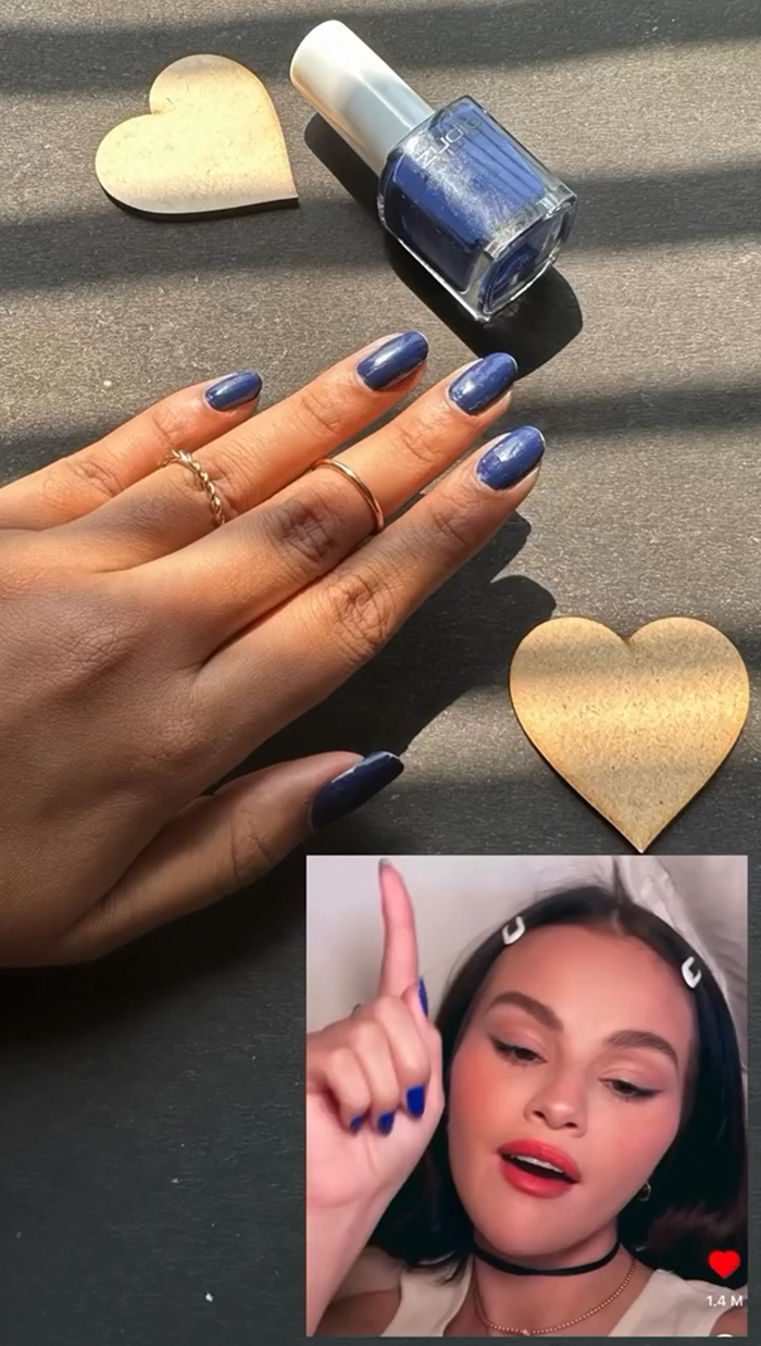 Hand with glossy blue nails next to matching nail polish bottle and decorative hearts, showcasing summer nails trends.