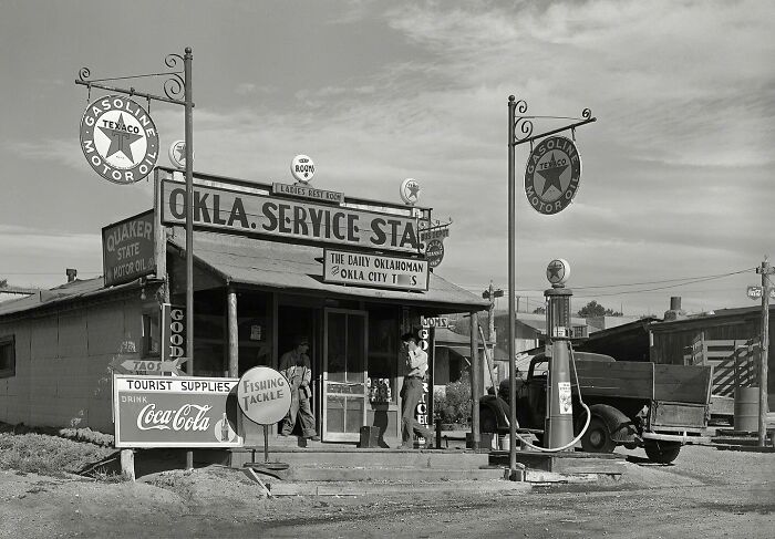 Colorized historical photo of an Oklahoma service station with vintage Texaco gasoline signs and people at the entrance.