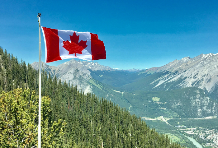 Canadian flag waving over mountain landscape, representing one of the best countries to live in 2025 rankings. Canadian flag waving over mountain landscape, representing one of the best countries to live in 2025 rankings.