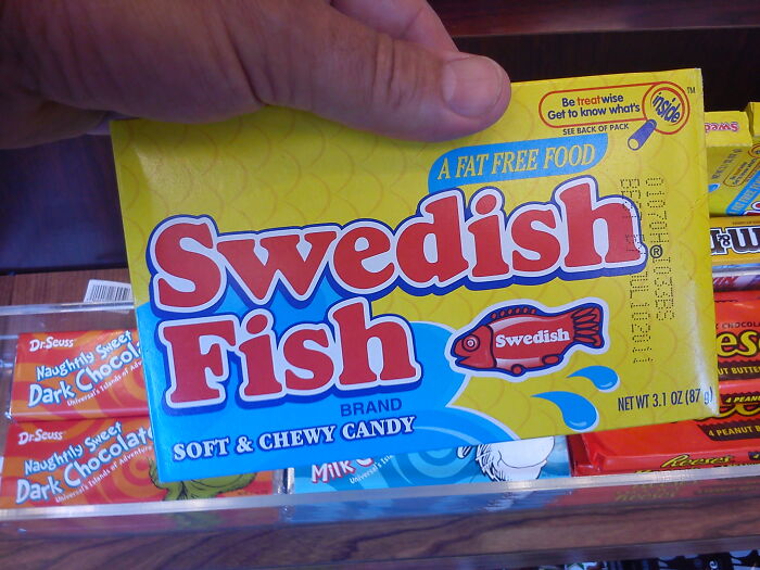 Hand holding a package of Swedish Fish candy, a soft and chewy treat in a colorful yellow and red box.