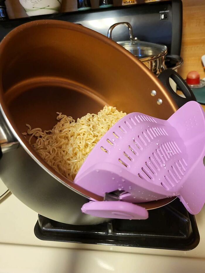 Copper nonstick pot with purple strainer draining noodles over a stove, best-selling kitchen items for easy cooking.