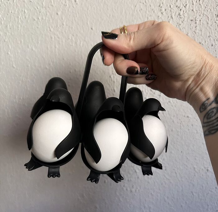 Hand holding a black penguin-shaped egg holder with white eggs, a unique best-selling kitchen item in use.