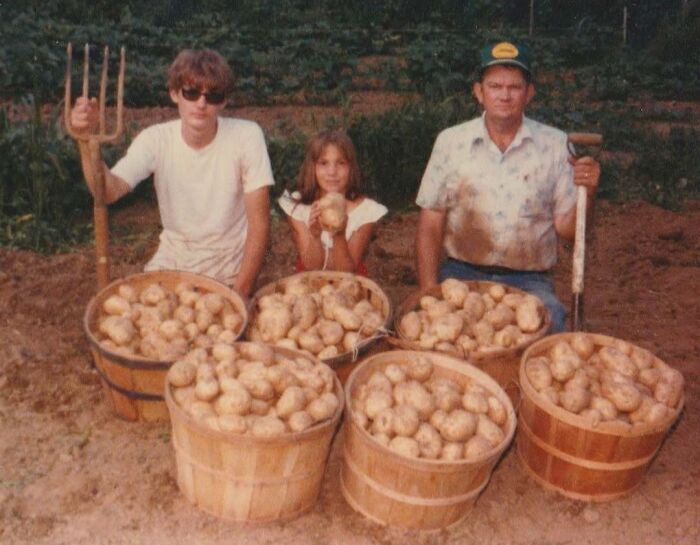 Vintage photo of a family proudly displaying a large harvest of potatoes in wooden baskets on a farm.