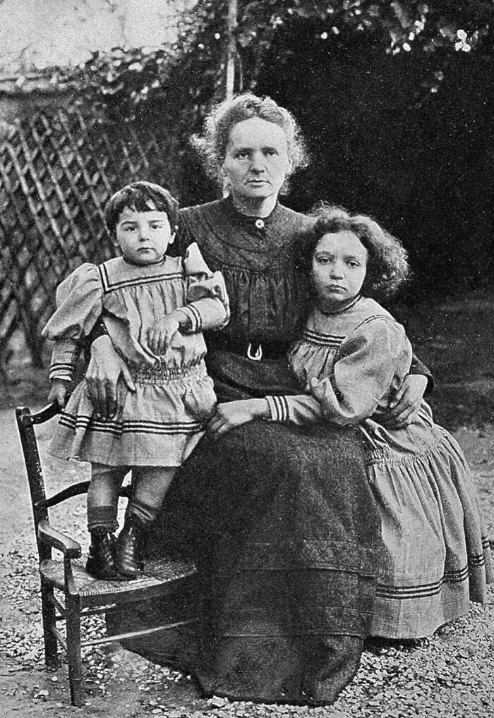 Marie Curie sitting outdoors with her two daughters in vintage clothing, a rare historical family portrait.