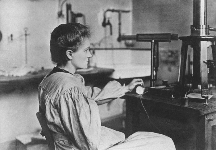 Marie Curie in a vintage laboratory setting, focused on scientific equipment during early radioactive research.