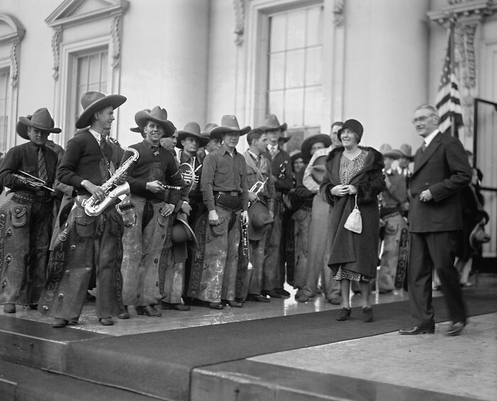Vintage cowboy band dressed in western attire with instruments, posing outside a historic building in the old West era.