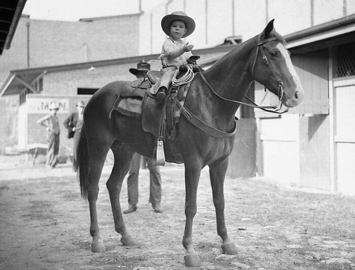 Young child dressed as a cowboy riding a horse in a vintage cowboy photograph from the Old West era.