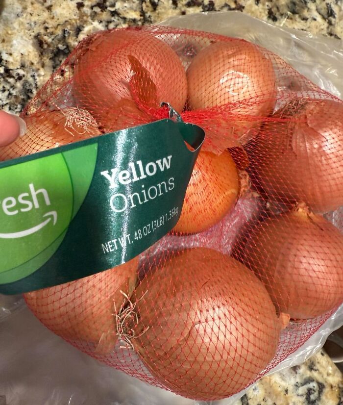 Bag of yellow onions labeled Amazon Fresh staples, highlighting cheaper alternatives to big box stores groceries.
