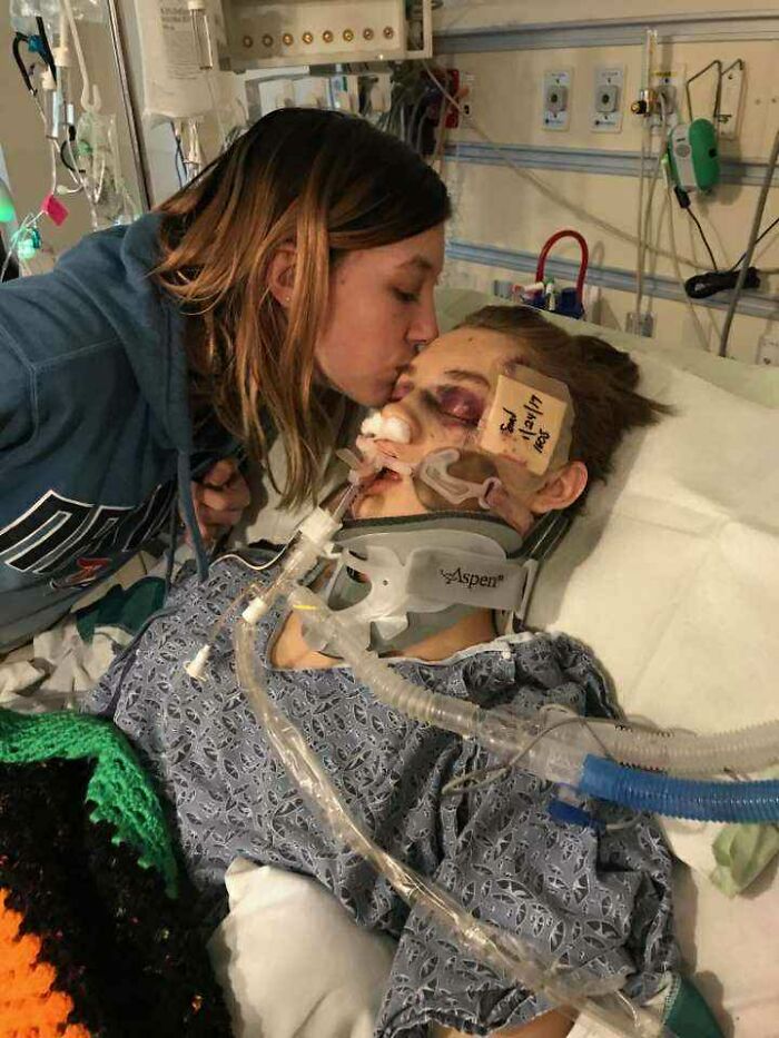 A woman kisses a young patient in a hospital bed with breathing tubes and a neck brace after a serious injury.