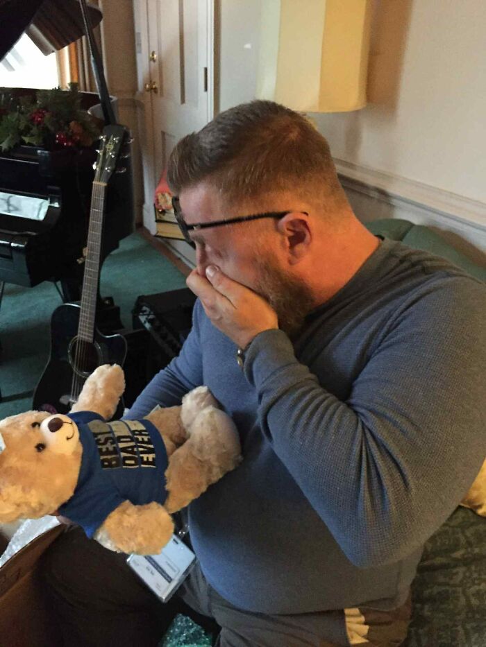 A dad emotional holding a teddy bear containing his late son's heartbeat in a cozy living room setting.