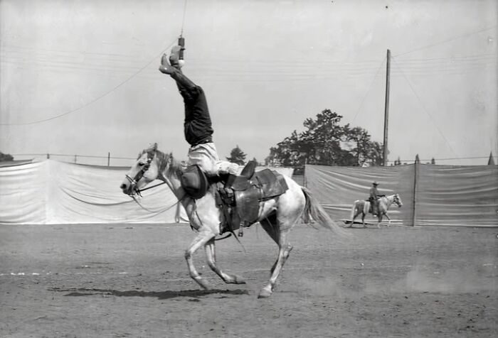 Vintage cowboy performing rodeo trick on horse in dusty arena, showcasing wild west skills from historic cowboy photographs.