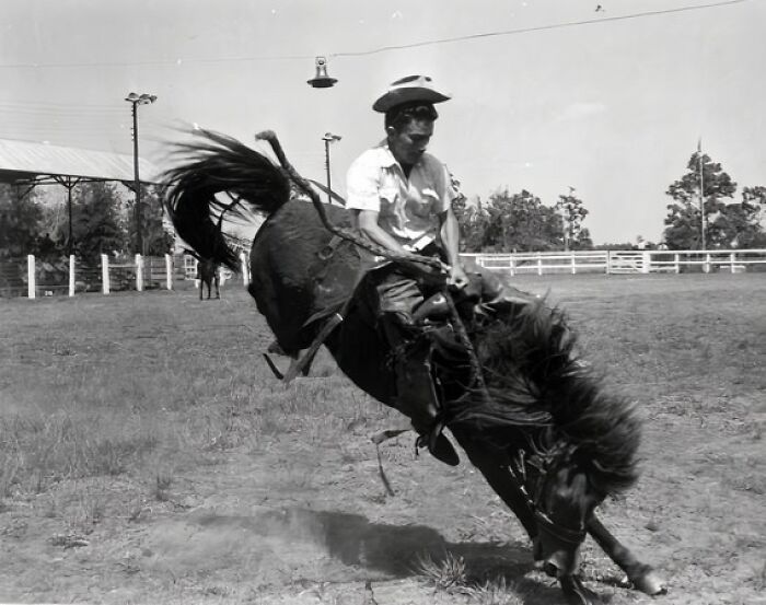 Vintage cowboy riding a bucking horse in an open field, showcasing classic western style and cowboy culture.