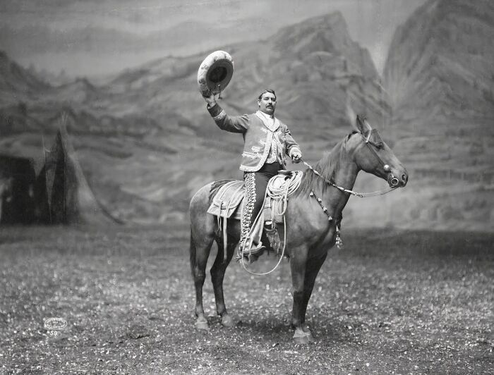 Vintage cowboy on horseback raising a hat in a scenic outdoor setting, showcasing historic Western life and culture.