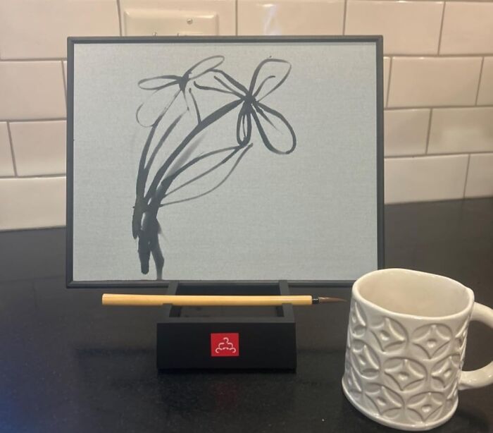Minimalist ink flower painting on a stand with brush placed below it, showcasing a popular crafting kit on a kitchen counter.