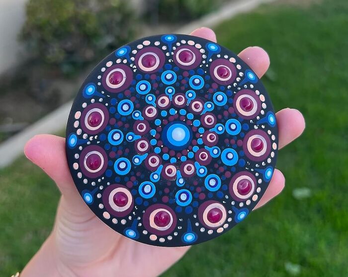 Hand holding a circular mandala dot painting in blue and purple colors, showcasing creative crafting kits.
