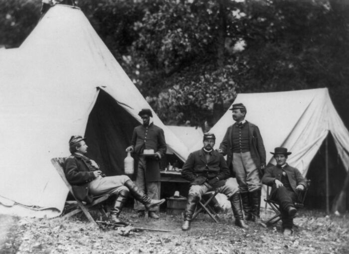 Group of Civil War soldiers resting near tents, highlighting African American military history in a camp setting.