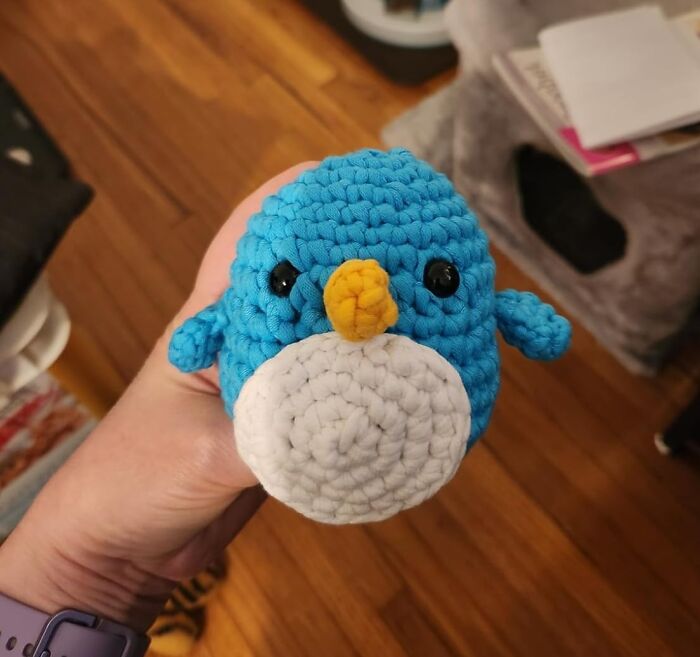 Hand holding a small crocheted blue bird with yellow beak, showcasing popular crafting kits for internet users.