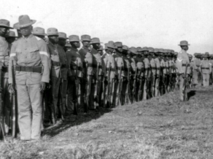 African American soldiers lined up in uniform holding rifles, representing African American military history.