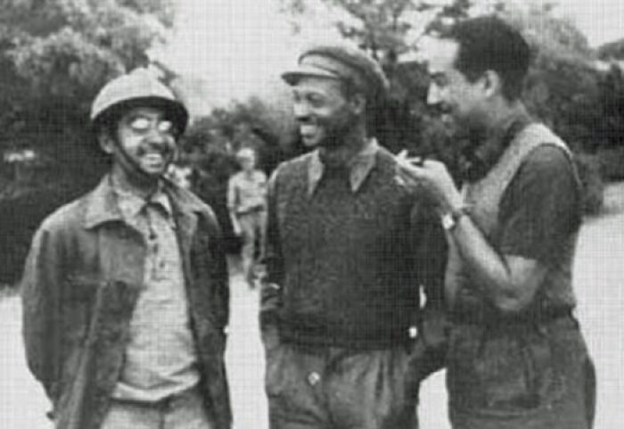 Three African American soldiers in WWII uniforms smiling and talking outdoors, highlighting African American military history.