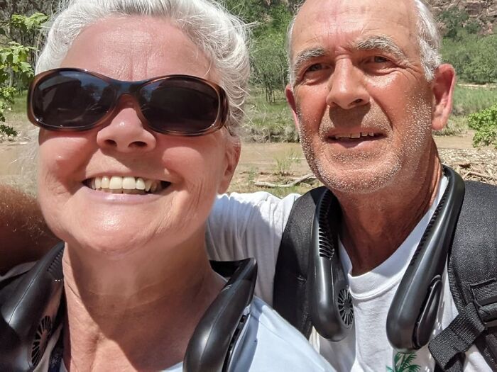 Older couple outdoors smiling, wearing portable neck fans to stop summer annoyances and stay cool.