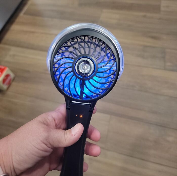 Hand holding a portable fan with blue blades spinning, a useful tool for beating summer annoyances effectively.