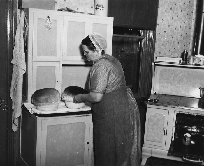 1940s housewife in apron and cap handling freshly baked bread in a vintage kitchen, showcasing iconic housewife life.