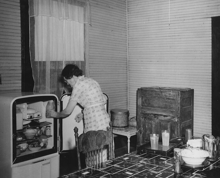 1940s housewife organizing food in a vintage kitchen, showcasing daily life and household tasks of the era.