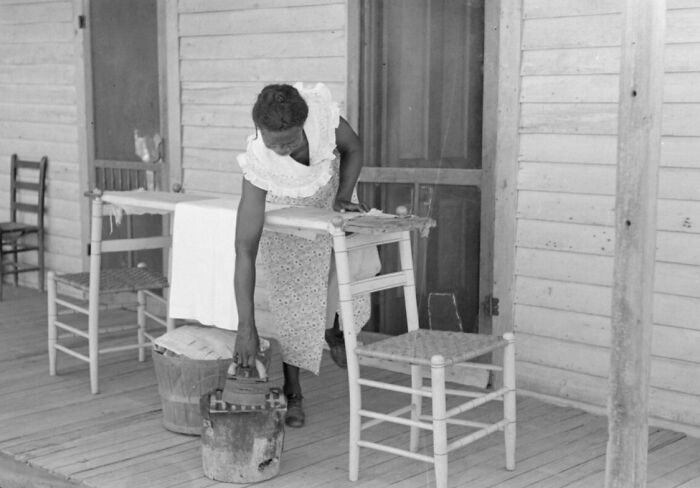 1940s housewife ironing clothes on porch, using charcoal iron, demonstrating daily life and household work.