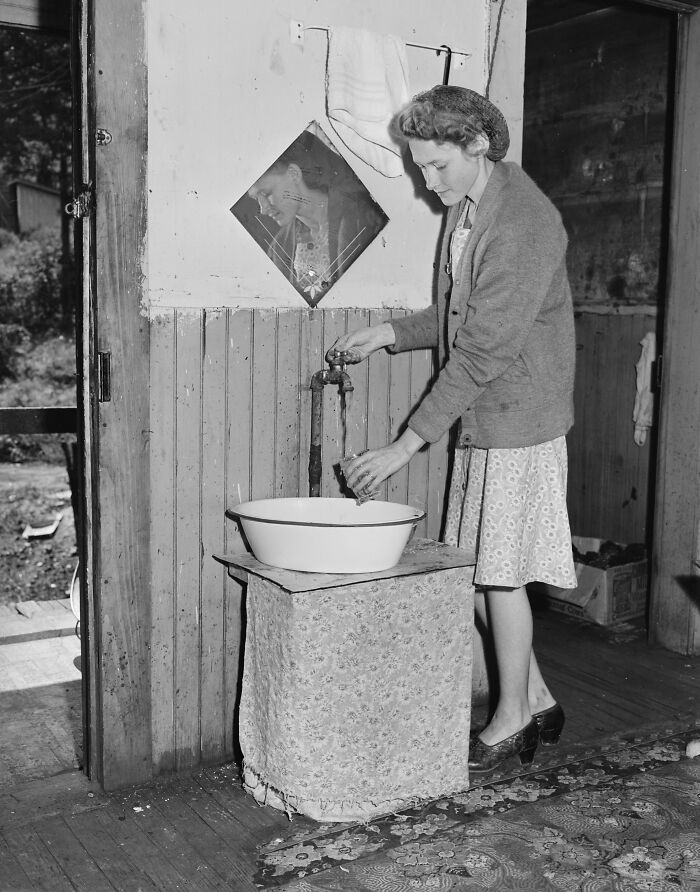 1940s housewife filling a glass with water from a tap indoors, showcasing daily life of iconic housewives of the era.