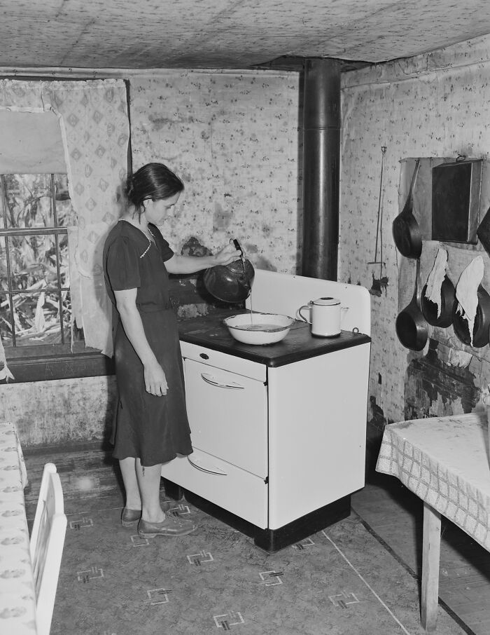 1940s housewife pouring batter in a rustic kitchen with vintage stove and cookware hanging on the wall.
