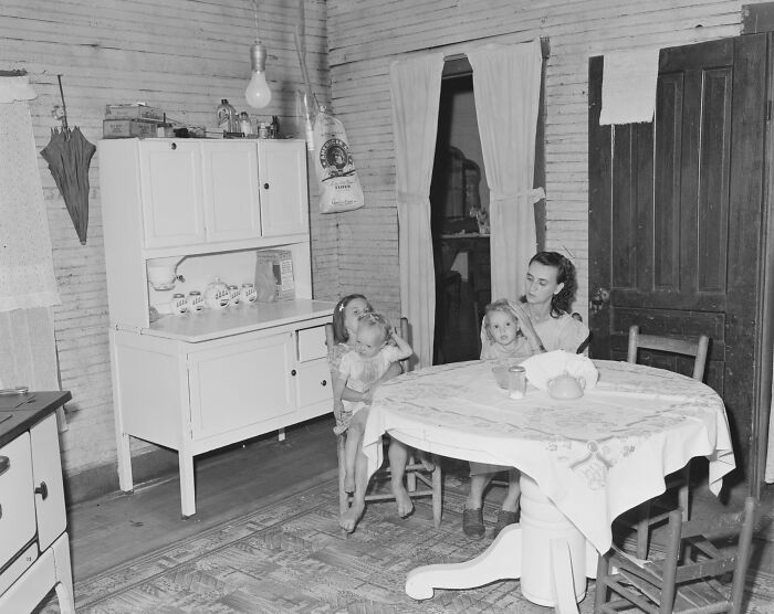 1940s housewife sitting at kitchen table with two children in a modest home, showcasing iconic family life of the era.