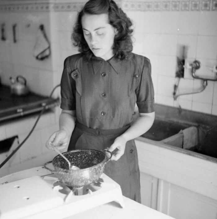1940s housewife cooking in a vintage kitchen, stirring food on a gas stove, reflecting iconic housewives who held the world together.