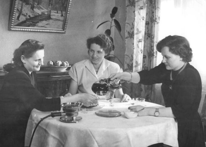 1940s housewives sitting around a table sharing tea in a cozy home setting, showcasing iconic daily life moments.