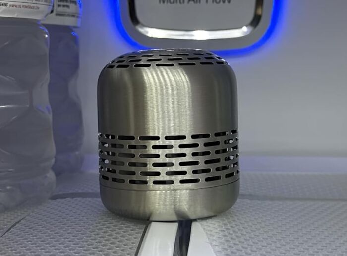 Stainless steel kitchen item with vent holes sitting on a textured surface near water bottles and an air flow vent.