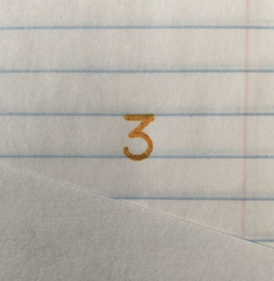 Close-up of a perfectly written number three in gold ink on lined notebook paper showcasing perfect handwriting examples.