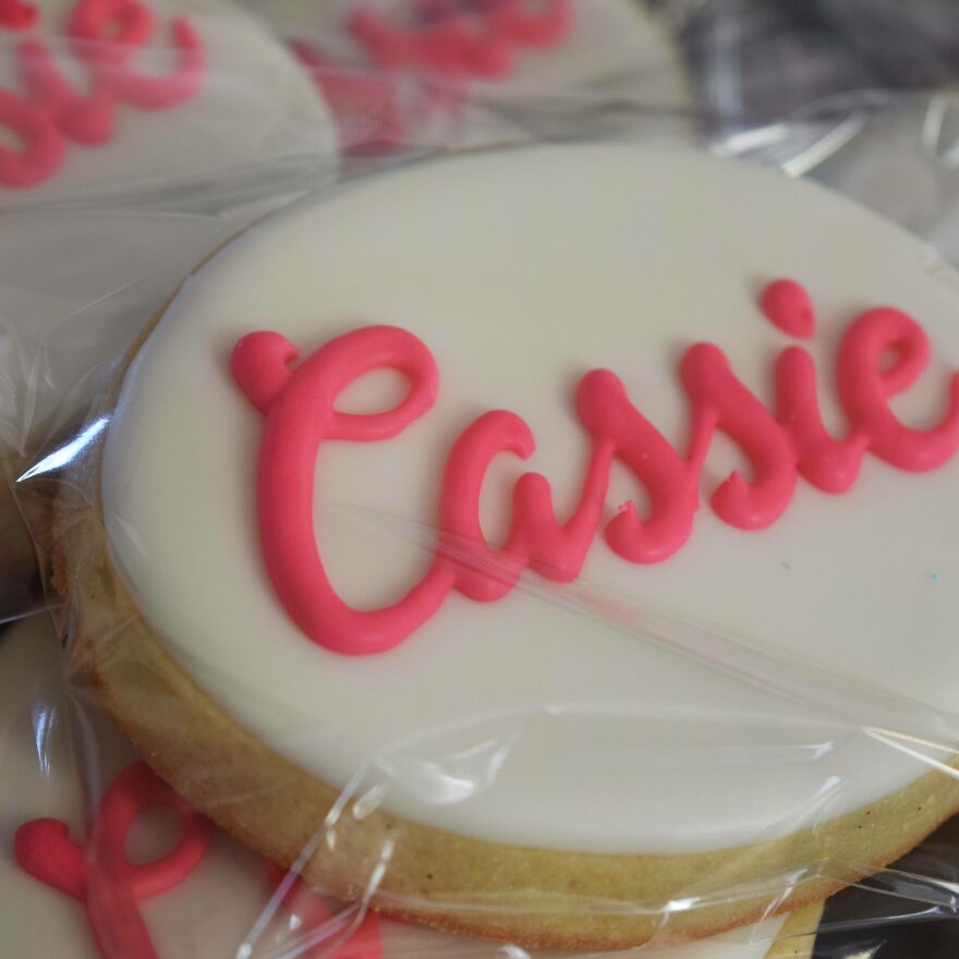 Close-up of a cookie with perfect handwriting in pink icing spelling Cassie on white icing background.
