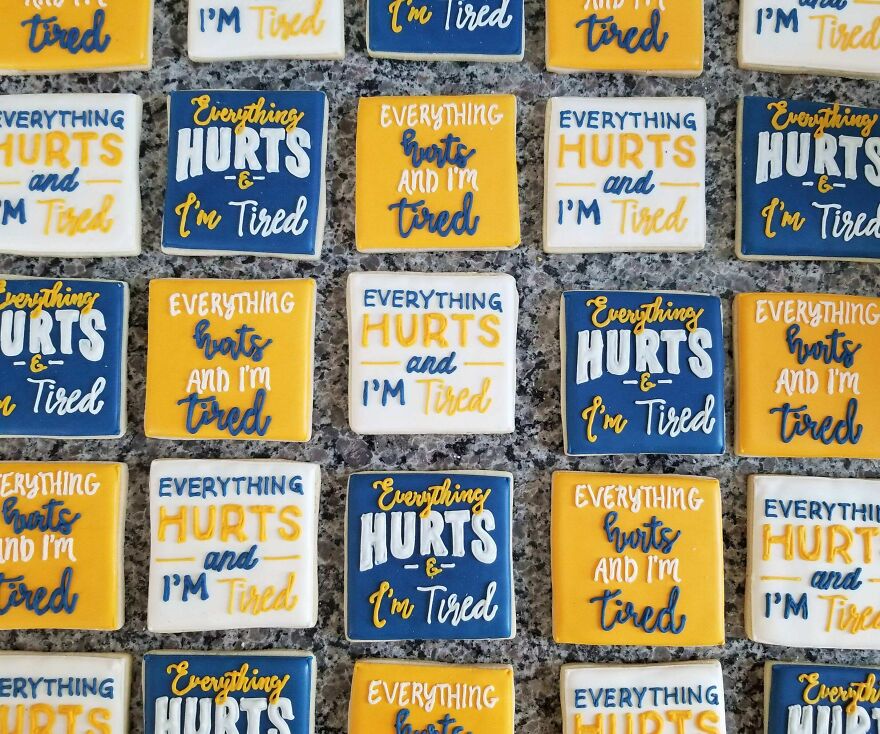 Cookies decorated with perfect handwriting spelling "Everything hurts and I'm tired" in blue, yellow, and white icing patterns.