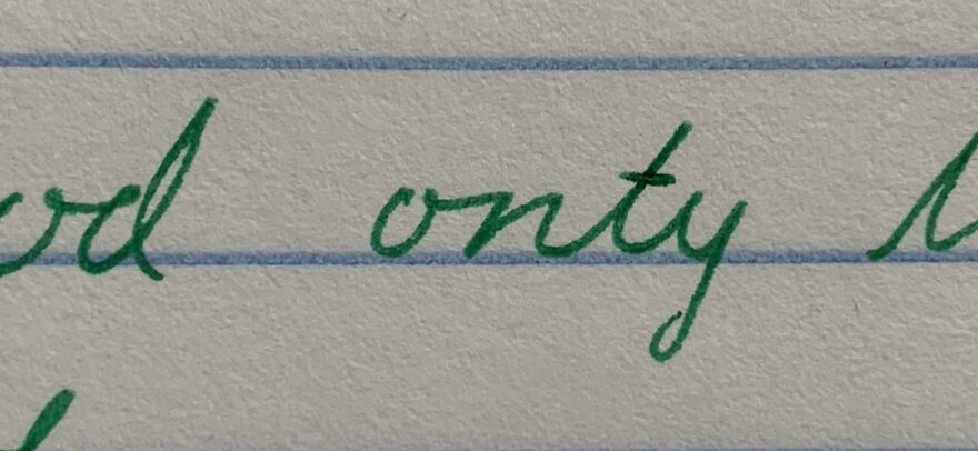 Close-up of perfect handwriting example in green ink on lined paper showcasing neat cursive style.