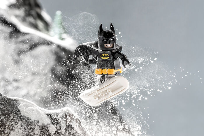 LEGO Batman minifigure snowboarding down a snowy slope in a detailed Hollywood-level LEGO scene by a photographer.