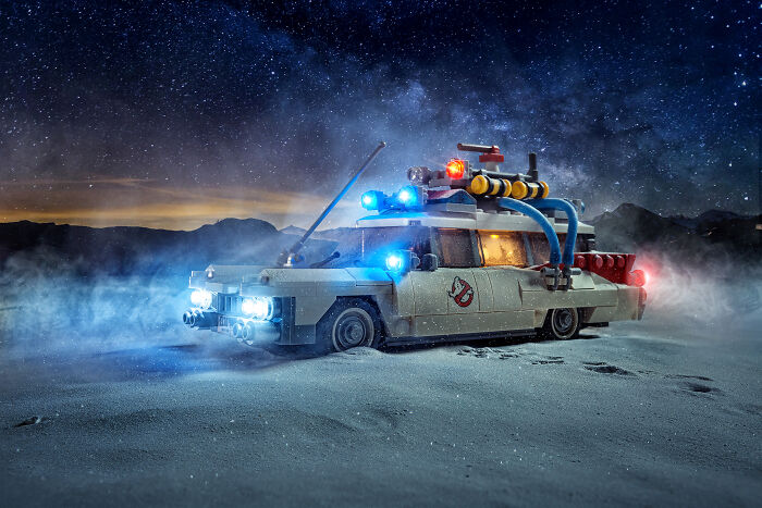 LEGO model of the Ghostbusters car with lights on, set in a dramatic nighttime scene with a starry sky.
