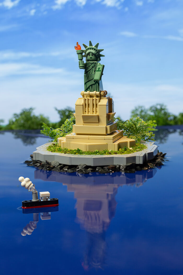 LEGO photographer creates a detailed Statue of Liberty scene with a miniature boat on reflective water, showcasing Hollywood-level artistry.
