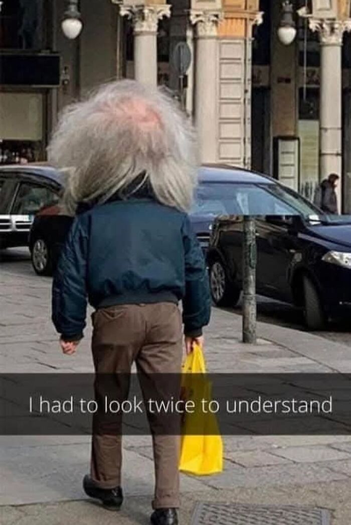 Person walking on city street with large fluffy white hair, holding yellow bag, funny meme about appearance confusion.
